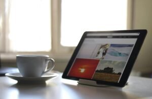 black tablet computer near a white ceramic teacup